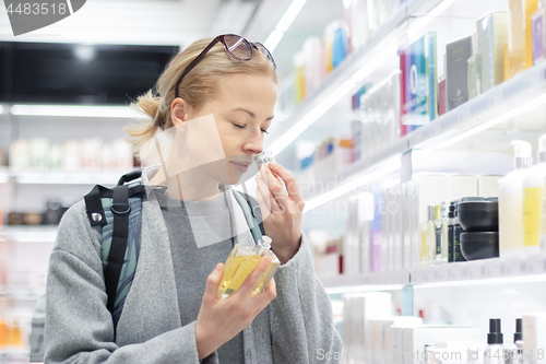 Image of Blond young female traveler wearing travel backpack choosing perfume in airport duty free store.