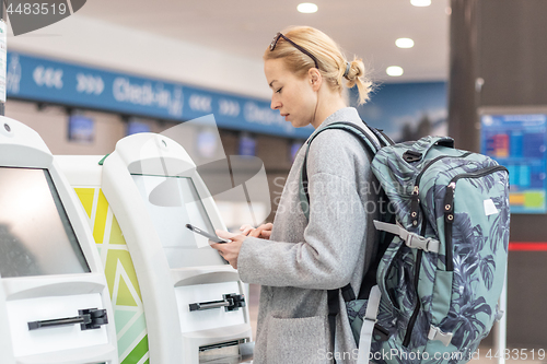 Image of Casual caucasian woman using smart phone application and check-in machine at the airport getting the boarding pass.