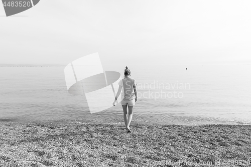 Image of Happy Carefree Woman Enjoying Sunset Walk on White Pabbled Beach.