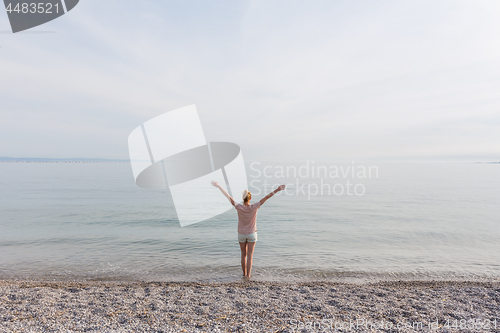 Image of Happy Carefree Woman Enjoying Sunset Walk on White Pabbled Beach.