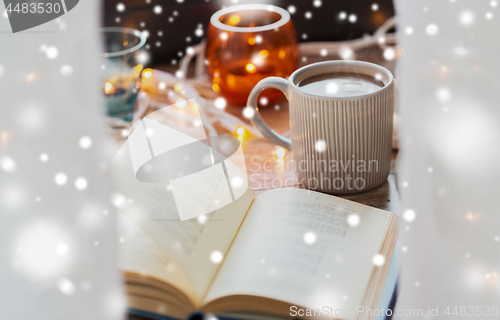 Image of book and cup of coffee or hot chocolate over snow