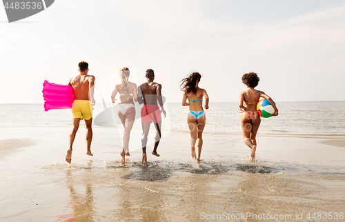 Image of friends run with beach ball and swimming mattress