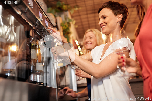 Image of happy women pouring wine from dispenser at bar