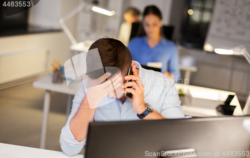 Image of stressed man calling on smartphone at night office