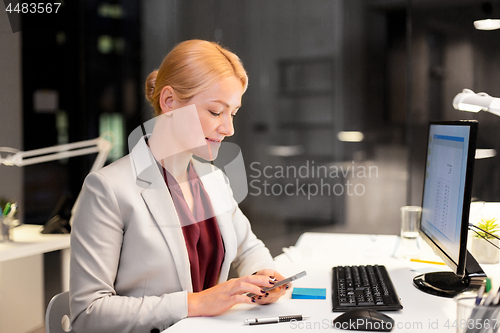 Image of businesswoman with smartphone at night office