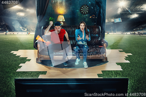 Image of Ardent fans are sitting on the sofa and watching TV in the middle of a football field.