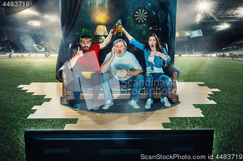 Image of Ardent fans are sitting on the sofa and watching TV in the middle of a football field.