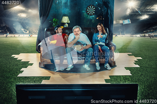 Image of Ardent fans are sitting on the sofa and watching TV in the middle of a football field.