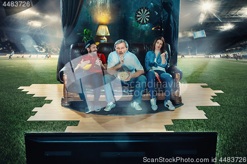 Image of Ardent fans are sitting on the sofa and watching TV in the middle of a football field.