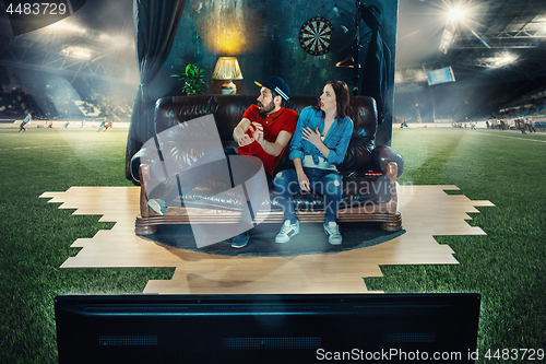 Image of Ardent fans are sitting on the sofa and watching TV in the middle of a football field.