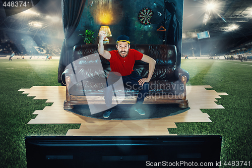 Image of Male fan sitting on the sofa and watching TV in the middle of a football field.