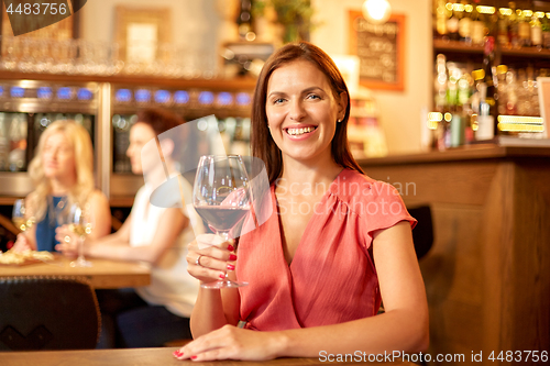 Image of happy woman drinking red wine at bar or restaurant