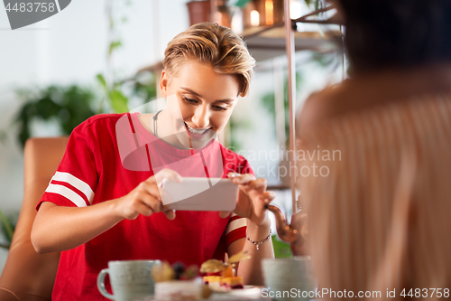 Image of happy woman photographing cake at cafe