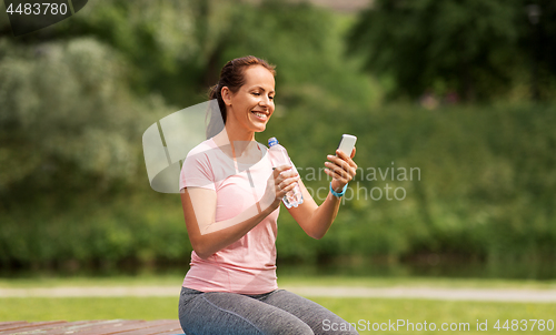 Image of woman with smartphone drinking water in park