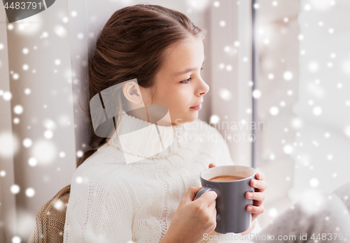 Image of girl in winter sweater with cacao mug at window