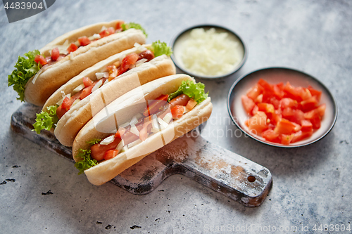 Image of Three barbecue grilled hot dogs with sausage placed on wooden cutting board