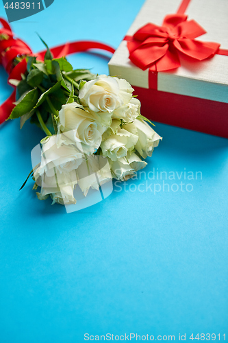 Image of Bouquet of white roses with red bow on blue background. Boxed gift on side