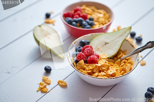 Image of Golden cornflakes with fresh fruits of raspberries, blueberries and pear in ceramic bowl