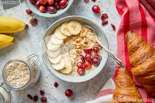 Image of Ceramic bowl of oatmeal porridge with banana, fresh cranberries and walnuts