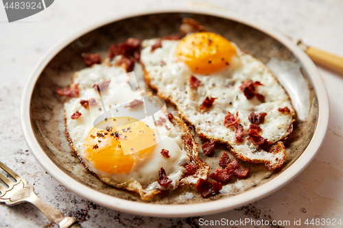 Image of Two fresh fried eggs with crunchy crisp bacon served on rustic plate