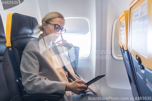 Image of Woman wearing glasses reading on digital e-reader while traveling by airplane.