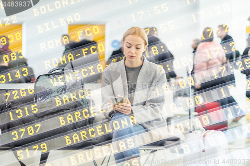 Image of Female traveler using her cell phone while waiting to board a plane at departure gates at airport terminal.