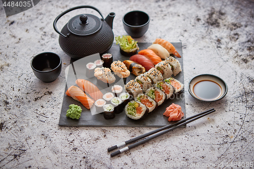 Image of Assortment of different kinds of sushi rolls placed on black stone board