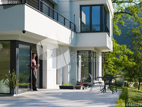 Image of man drinking coffee in front of her luxury home villa