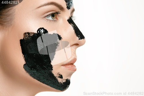 Image of Young beautiful woman applying a mask for the face of the therapeutic black mud. Spa treatment