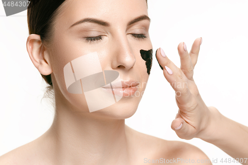 Image of Young beautiful woman applying a mask for the face of the therapeutic black mud. Spa treatment