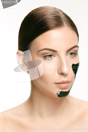 Image of Young beautiful woman applying a mask for the face of the therapeutic black mud. Spa treatment