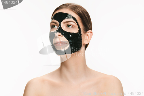 Image of Young beautiful woman applying a mask for the face of the therapeutic black mud. Spa treatment