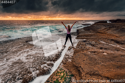 Image of Spirited girl standing over rock crevice as waves wash in