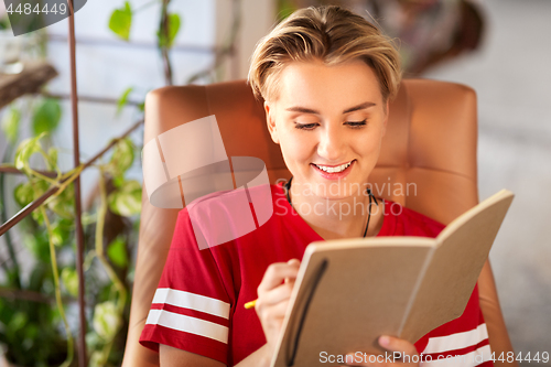 Image of happy teenage girl writing to notebook at cafe