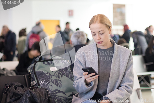 Image of Female traveler reading on her cell phone while waiting to board a plane at departure gates at airport terminal.