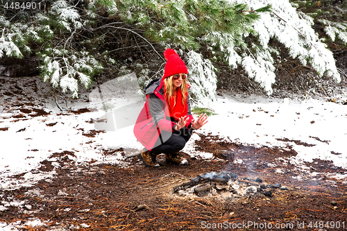 Image of Girl crouching and warming frost bite hands in the smouldering fire