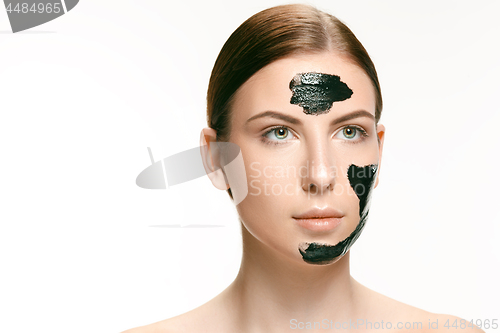 Image of Young beautiful woman applying a mask for the face of the therapeutic black mud. Spa treatment