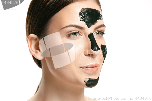 Image of Young beautiful woman applying a mask for the face of the therapeutic black mud. Spa treatment