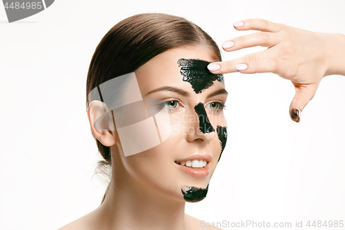 Image of Young beautiful woman applying a mask for the face of the therapeutic black mud. Spa treatment