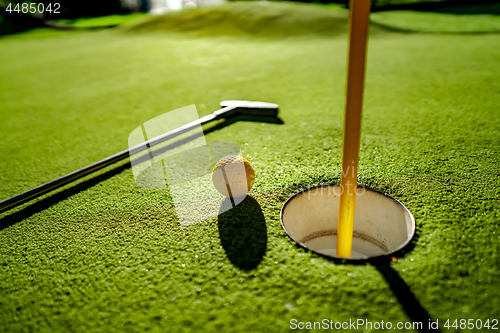 Image of Mini Golf yellow ball with a bat near the hole at sunset