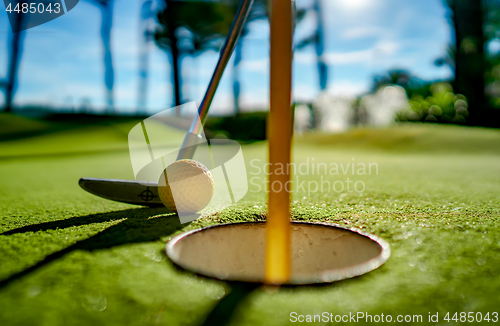 Image of Mini Golf yellow ball with a bat near the hole at sunset