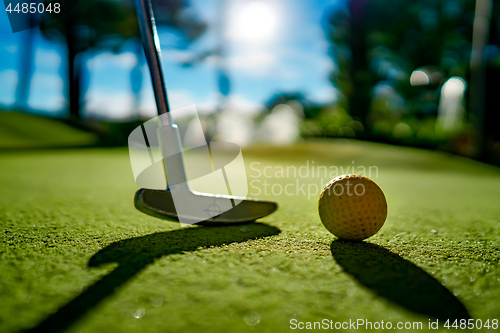 Image of Mini Golf yellow ball with a bat near the hole at sunset