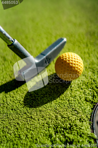 Image of Mini Golf yellow ball with a bat near the hole at sunset