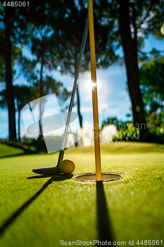 Image of Mini Golf yellow ball with a bat near the hole at sunset