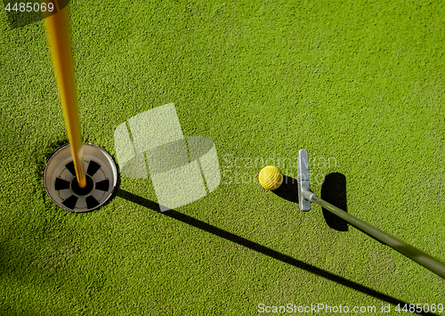 Image of Mini Golf yellow ball with a bat near the hole at sunset