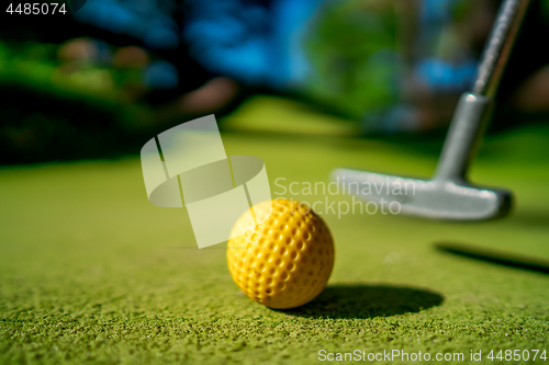 Image of Mini Golf yellow ball with a bat near the hole at sunset