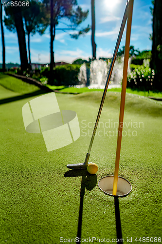 Image of Mini Golf yellow ball with a bat near the hole at sunset