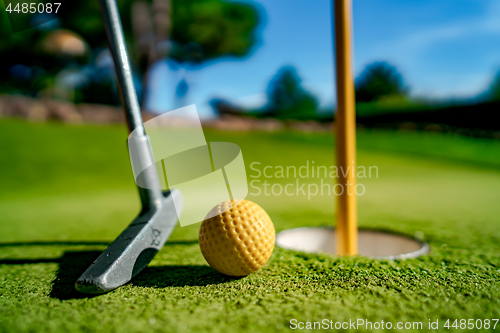 Image of Mini Golf yellow ball with a bat near the hole at sunset