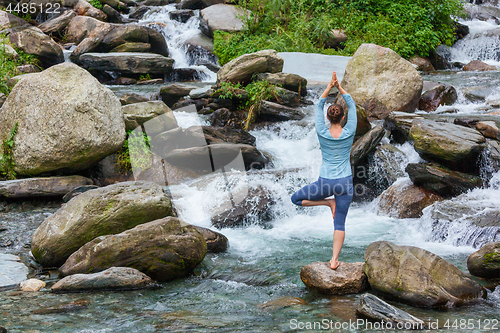 Image of Woman in yoga asana Vrikshasana tree pose at waterfall outdoors