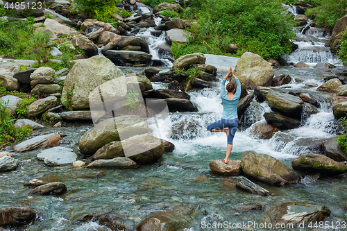 Image of Woman in yoga asana Vrikshasana tree pose at waterfall outdoors